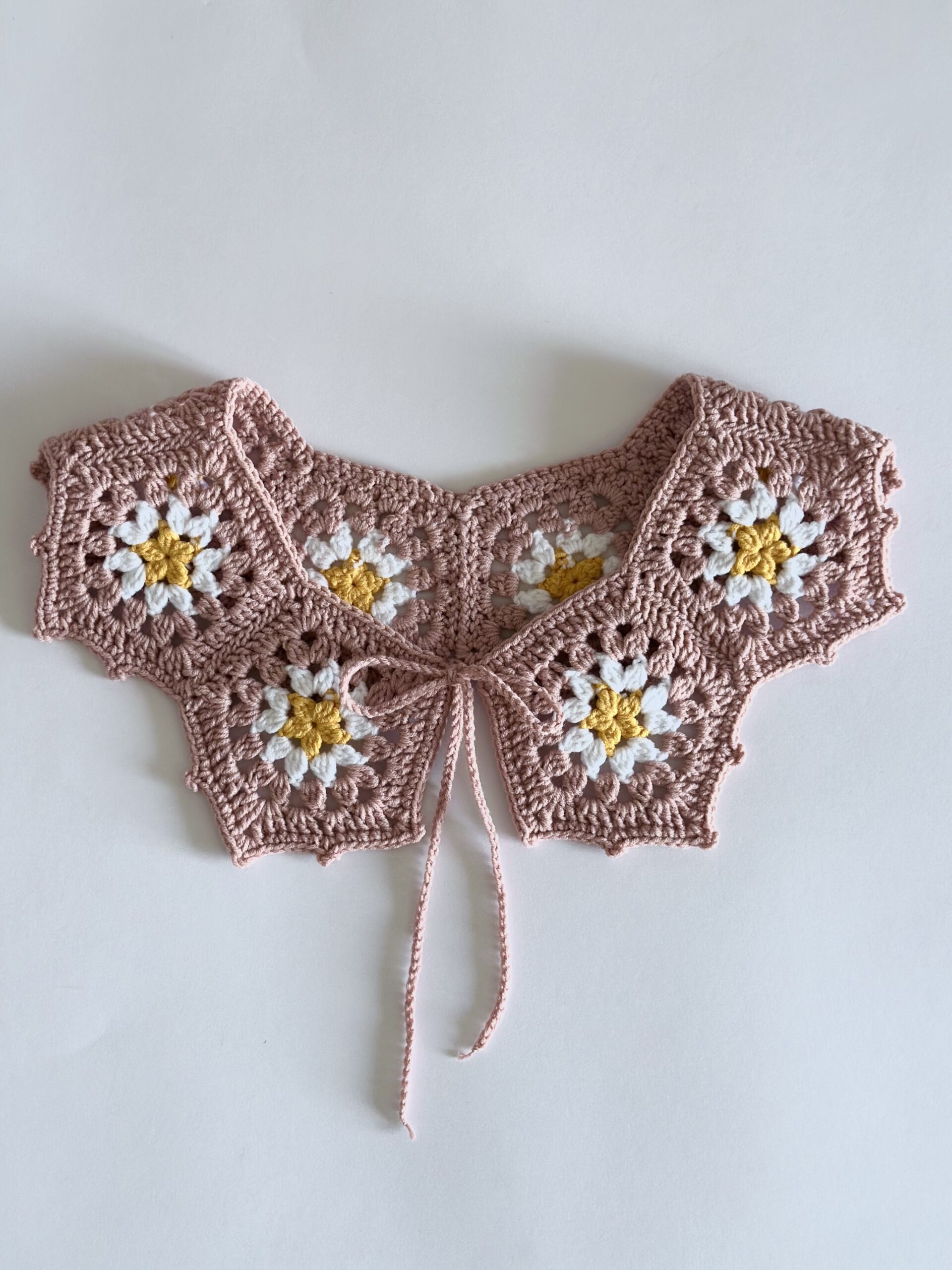 ażurowy kołnierzyk wykonany na szydełku. wiązany na troczki. kolor to pudrowy róż ze stokrotką pośrodku.