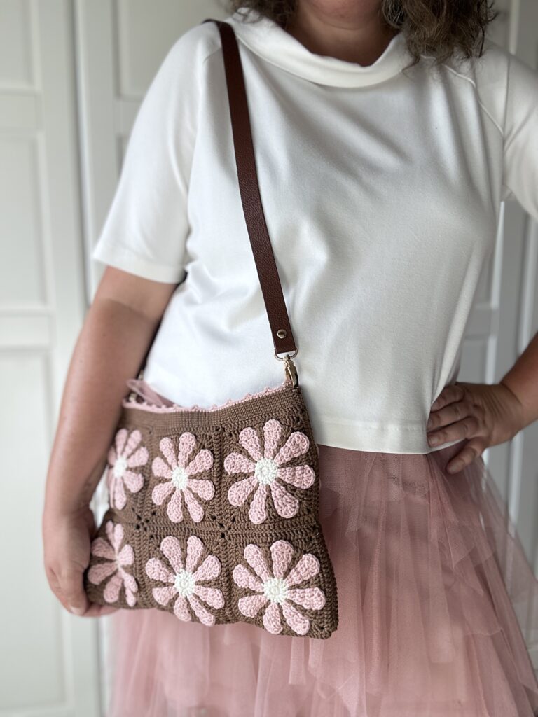 Szydełkowa torebka w retro kwiaty. kolory to czekoladowy brąz i pudrowy róż z dodatkiem jasnego beżu. Torebka ma regulowany pasek ze skóry naturalnej, co pozwala nosić ją na dwa sposoby - na ramieniu lub przez głowę. torba ma bawełnianą podszewkę i jest zapinana na zamek błyskawiczny. Po odpięciu paska torebkę można prać w pralce.
