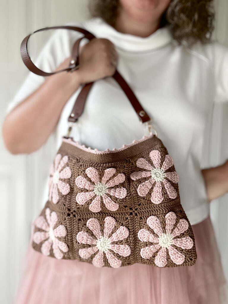 Szydełkowa torebka w retro kwiaty. kolory to czekoladowy brąz i pudrowy róż z dodatkiem jasnego beżu. Torebka ma regulowany pasek ze skóry naturalnej, co pozwala nosić ją na dwa sposoby - na ramieniu lub przez głowę. torba ma bawełnianą podszewkę i jest zapinana na zamek błyskawiczny. Po odpięciu paska torebkę można prać w pralce.