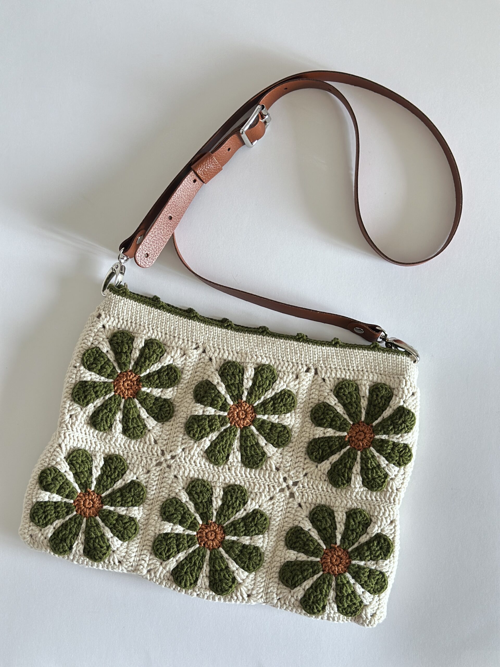 niepowtarzalna torebka wykonana na szydełku. torebka jest w beżowym kolorze w kwiaty w kolorze oliwkowym. ma podszewkę z kieszonką, jest zapinana na zamek. posiada skórzany pasek z możliwością regulacji długości. idealna na co dzień.