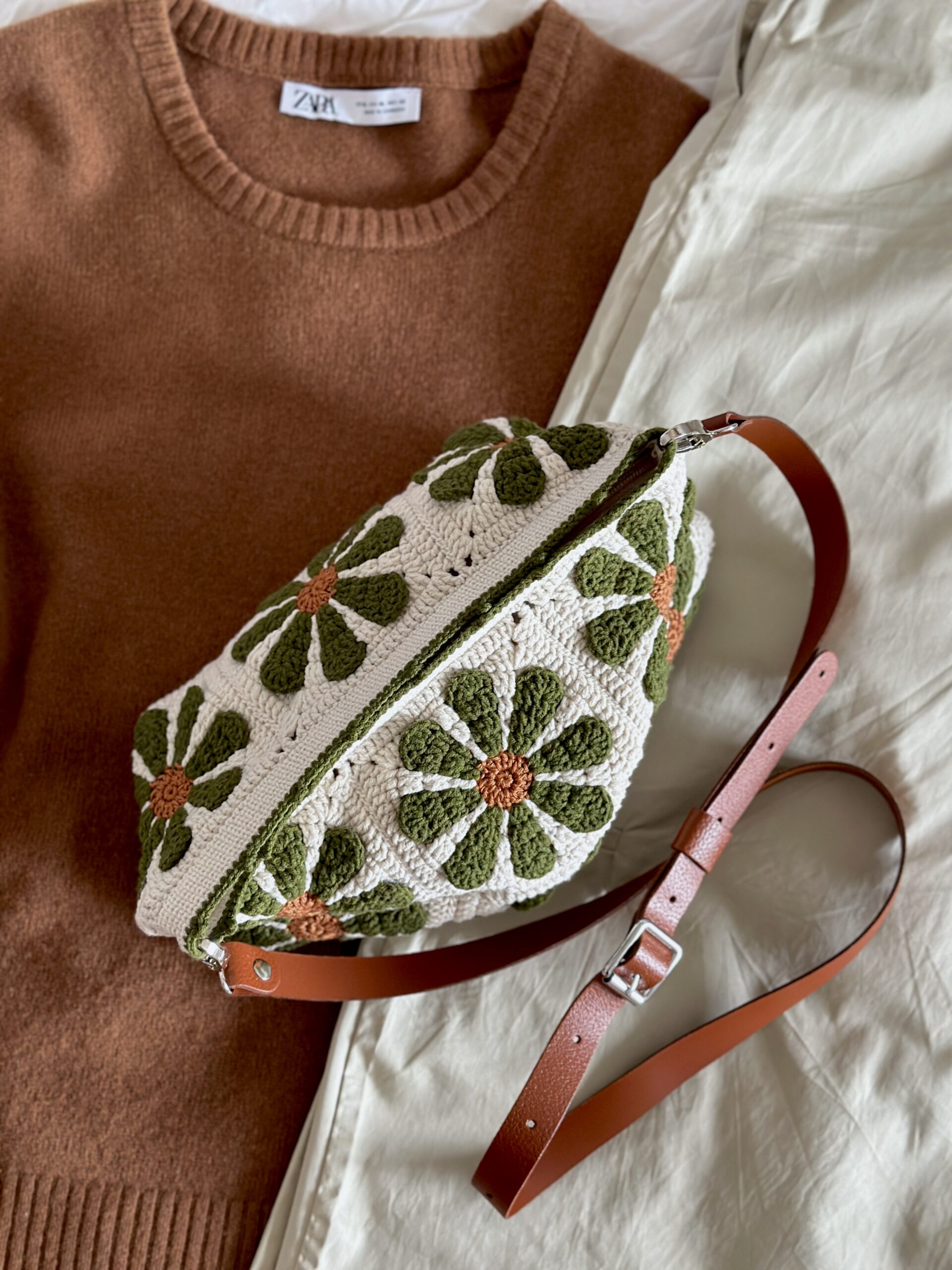 dziergana torebka w retro kwiaty. tło beżowe, kwiaty miedziano oliwkowe. torebka ma pasek ze skóry naturalnej z możliwością regulacji długości. posiada również podszewkę z kieszonką i jest zapinana na zamek błyskawiczny. jest to polskie rękodzieło