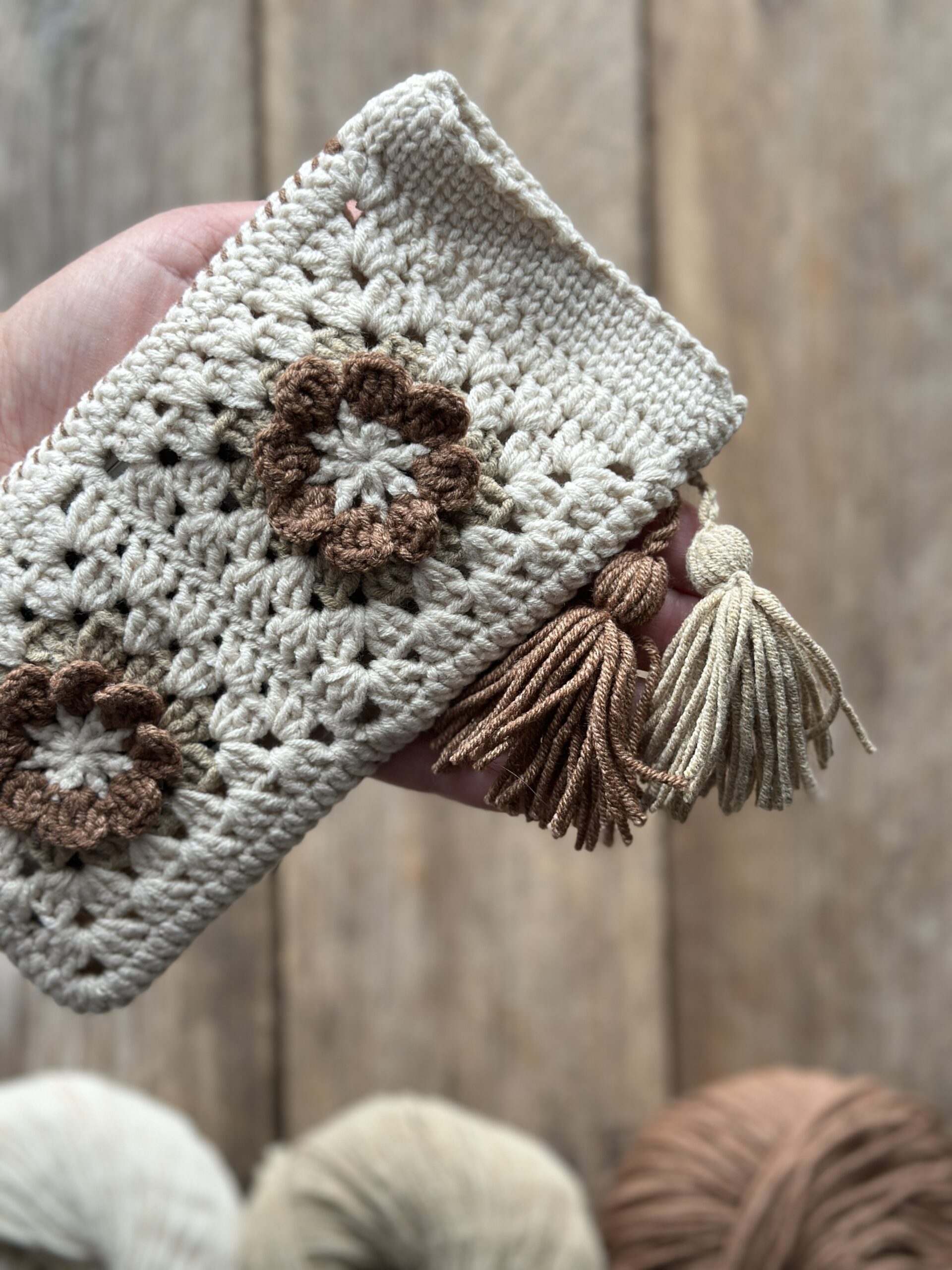szydełkowe etui na telefon lub okulary, zapinane na zapięcie magnetyczne, ozdobione dwoma chwostami. kolor dominujący to jasny beż, dodatkowo brąz i ciemny beż.