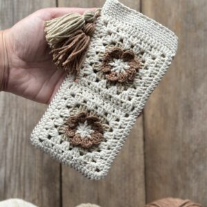 szydełkowe etui na telefon lub okulary, zapinane na zapięcie magnetyczne, ozdobione dwoma chwostami. kolor dominujący to jasny beż, dodatkowo brąz i ciemny beż.