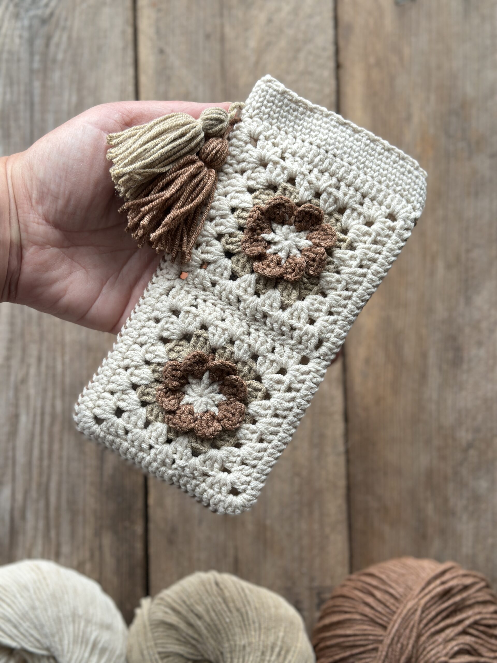 szydełkowe etui na telefon lub okulary, zapinane na zapięcie magnetyczne, ozdobione dwoma chwostami. kolor dominujący to jasny beż, dodatkowo brąz i ciemny beż.