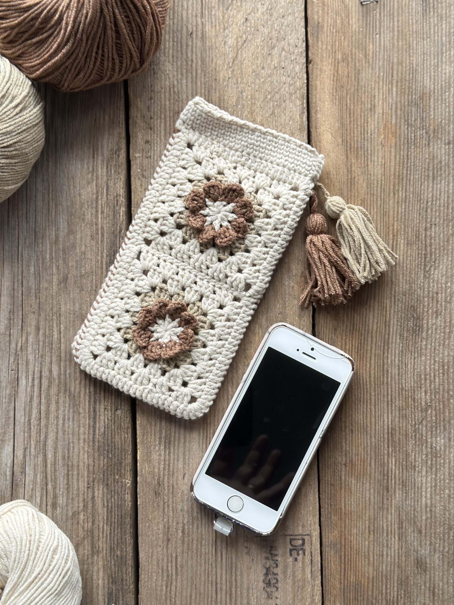 szydełkowe etui na telefon lub okulary, zapinane na zapięcie magnetyczne, ozdobione dwoma chwostami. kolor dominujący to jasny beż, dodatkowo brąz i ciemny beż.