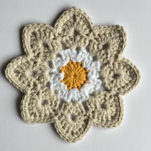 Podkładka pod kubek ręcznie wykonana na szydełku, kwiatowy design, neutralne odcienie beżu, bieli i żółtego.